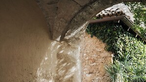 A stone bench with cushions under a stone archway, surrounded by cobblestone ground and greenery. - Ansitz Zinnenberg (Appiano Sulla Strada del Vino)