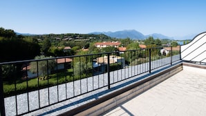 Ein Balkon mit Metallgeländer, der auf einen Wohnbereich mit Häusern und Bergen im Hintergrund blickt.