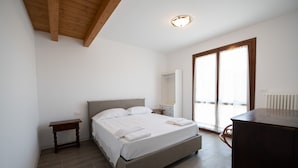 Ein Schlafzimmer mit Bett, Nachttisch, Schminktisch und Blick ins Freie durch eine Schiebetür.