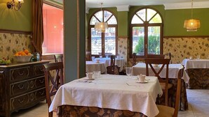 A dining area with tables set for two, a wooden buffet with fruit, and large windows with arched tops. - Vivienda 2 Personas Finca Malvasia (Cabezón de Liébana)