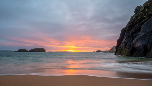 A beach with calm waters and a sunset.