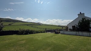 A rural landscape with a white house, green fields, and a clear sky.