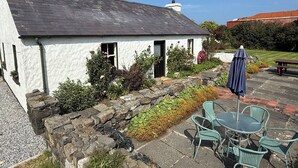 A white cottage with a stone wall and a tiled patio.