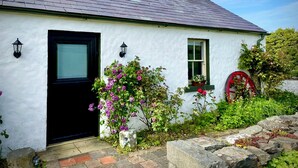 A white cottage with a black door, a small window, and a chimney.