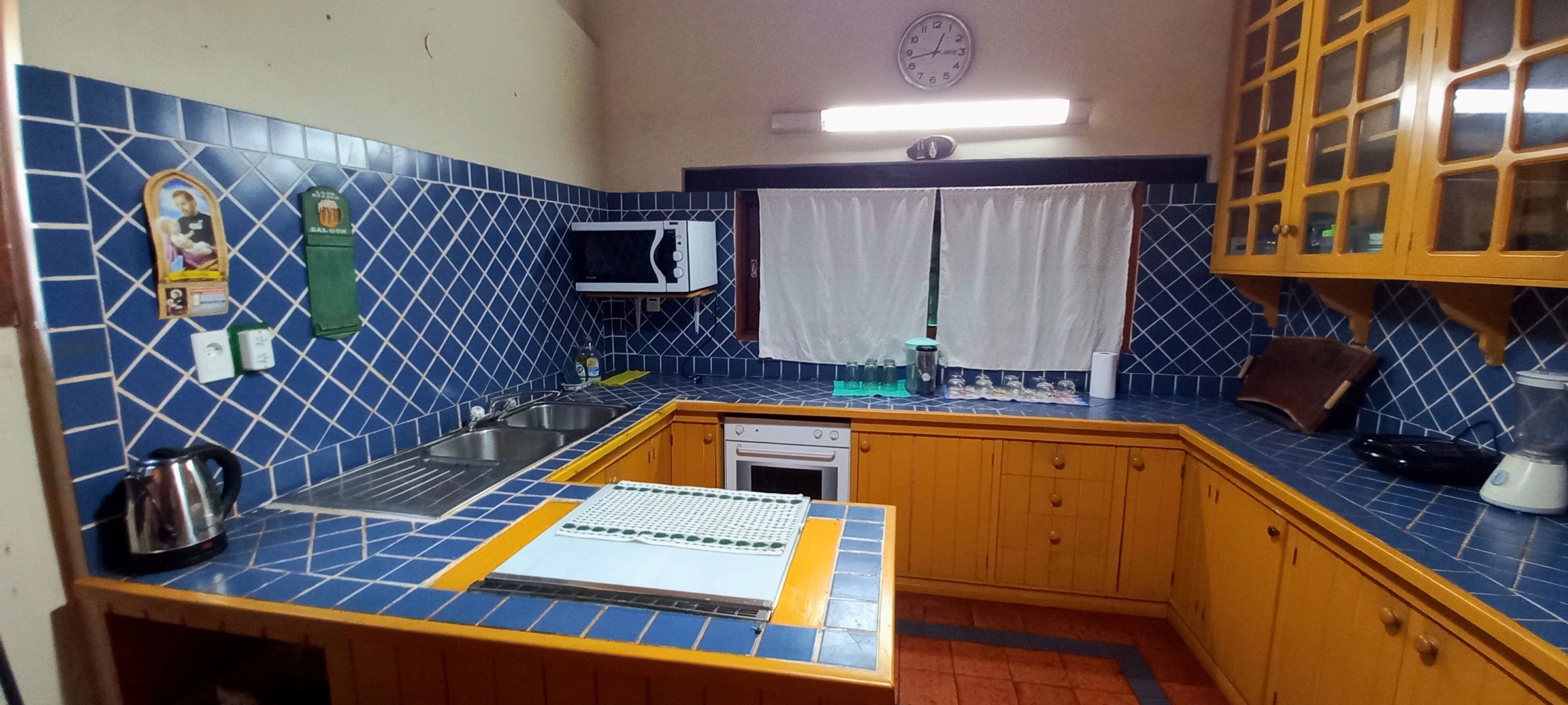 A kitchen with blue and yellow tiled walls, a microwave, sink, and wooden cabinets.