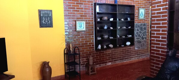 A room with a brick wall, a yellow wall, and a shelf with pottery.