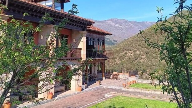 A two-story building with a balcony, surrounded by a well-maintained lawn and a mountainous backdrop.