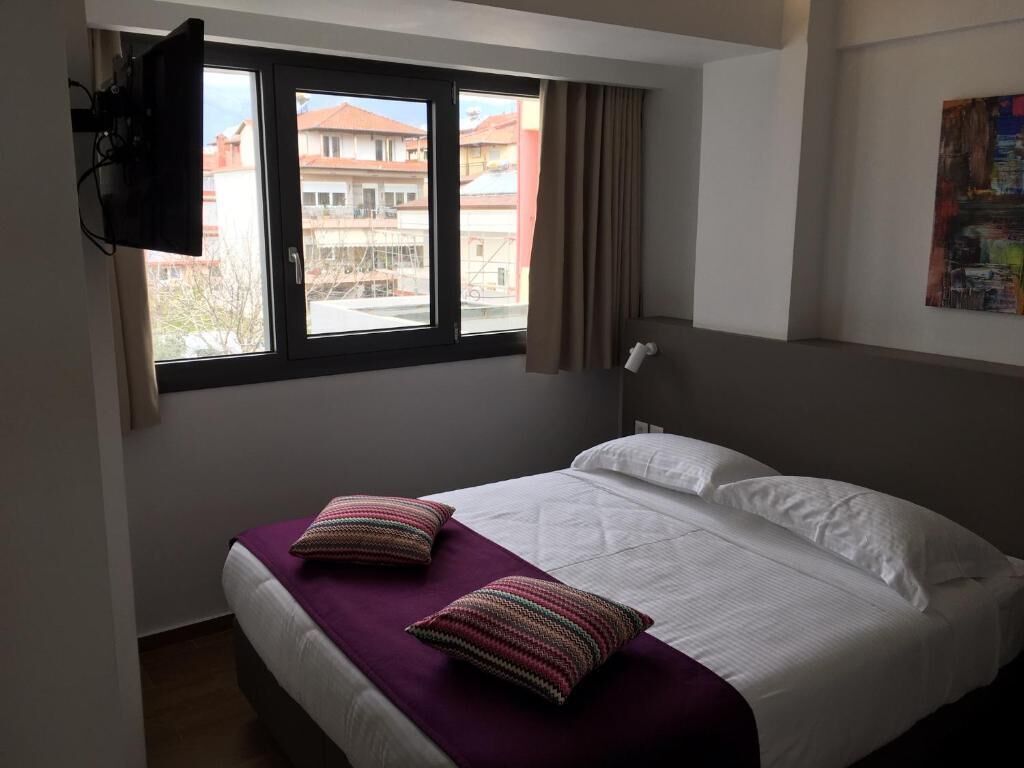 A hotel room with a bed, a window, and a television.