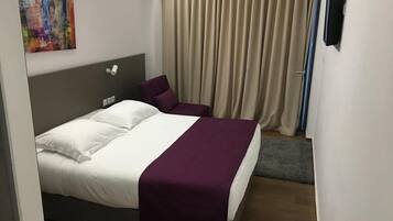 Una habitación de hotel con cama, cabecera, almohada, manta, un cuadro en la pared y cortina.