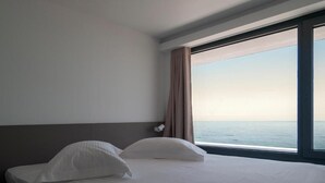 Una habitación de hotel con una cama, una mesita de noche, un ventanal con vistas al mar y una cortina.