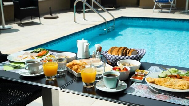 Desayuno junto a la piscina, con una variedad de platos como croissants, huevos y fruta, además de bebidas y una cafetera.