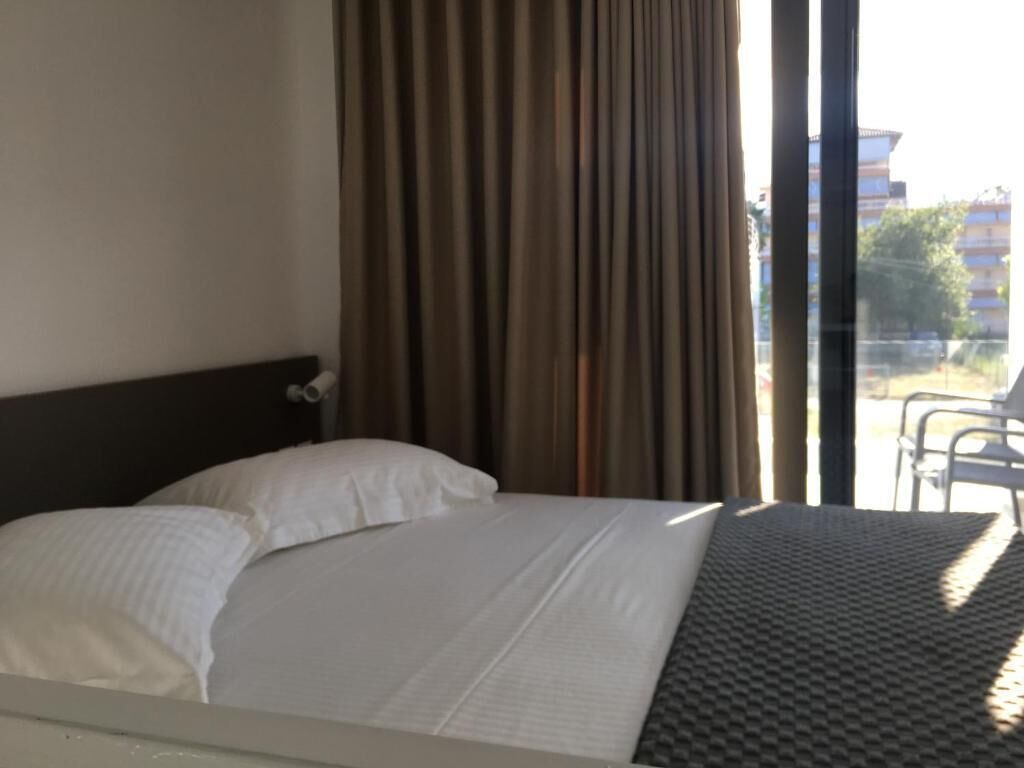 A hotel room with a bed, a window with curtains, and a view of the outside.