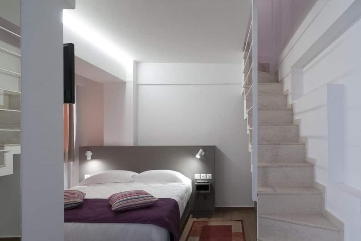 Un dormitorio moderno con una cama, lámparas de noche, una mesita de noche y una escalera.