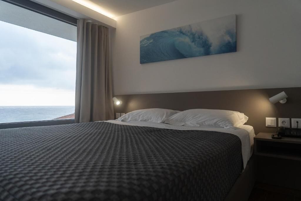 Une chambre d’hôtel avec un grand lit, une vue sur la mer, un tableau au mur et une table de chevet avec une lampe.