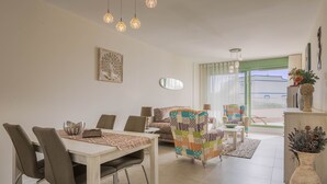 A modern living room with a dining area, a colorful armchair, and a large window with a view.