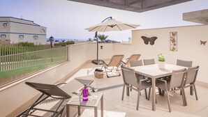 A balcony with a dining table, chairs, and a sun umbrella.