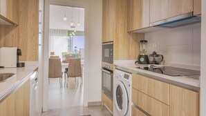 A modern kitchen with wooden cabinets, a built-in dishwasher, a washing machine, and a coffee maker.