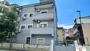 Un edifici residencial de diversos pisos amb façana gris, aparells d'aire condicionat i entrada tancada per una reixa.