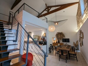 Stunning interior with a high ceiling, central staircase, and modern dining area featuring a wooden table and flat-screen TV.