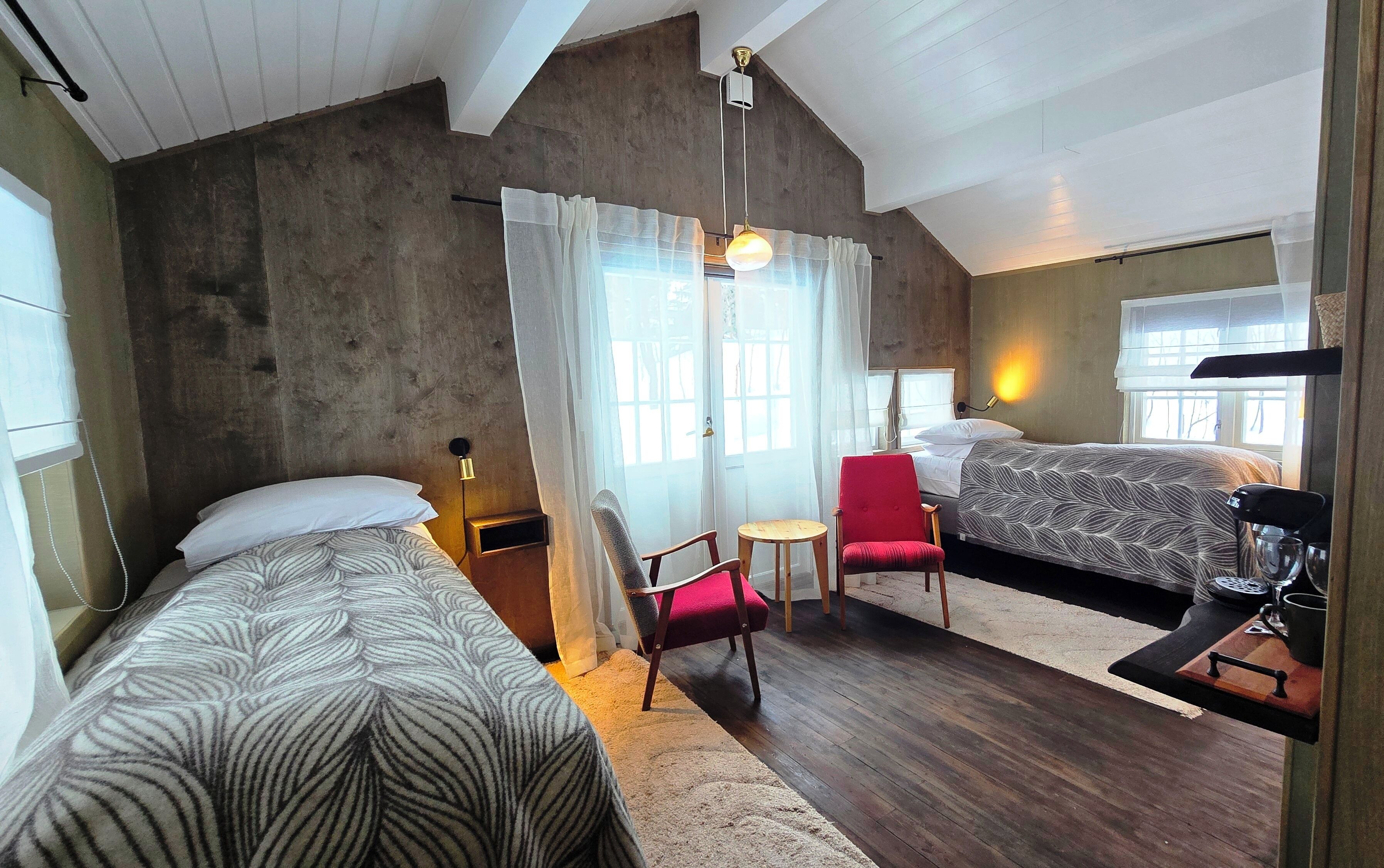A bedroom with two beds, a red chair, a small table, and a ceiling light.