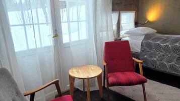 A room with a bed, a red chair, a wooden chair, a small round table, and a hanging light fixture.