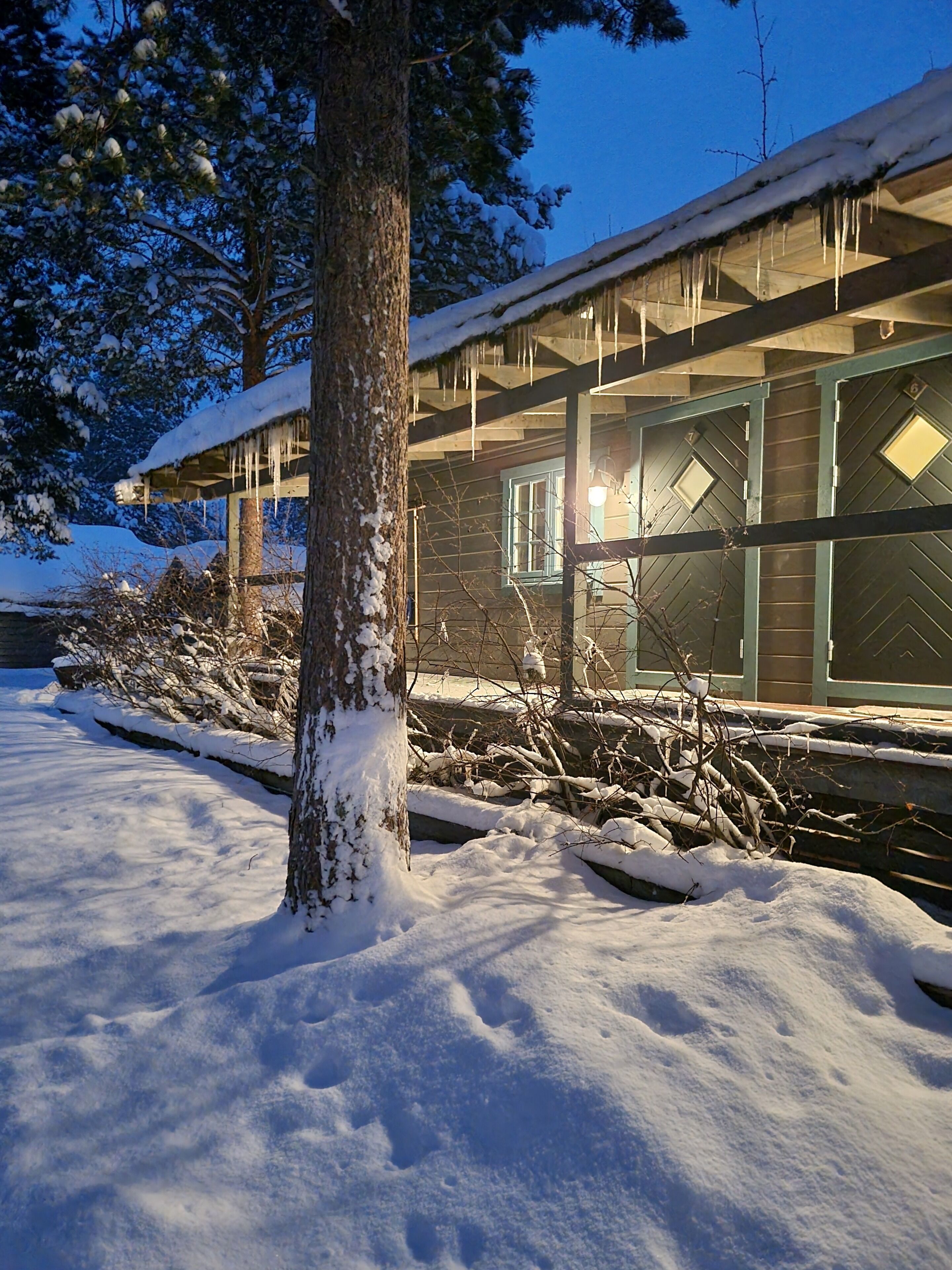 A snow-covered landscape with a wooden building featuring large windows and a covered porch.