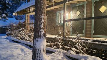 A snow-covered landscape with a wooden building featuring large windows and a covered porch.