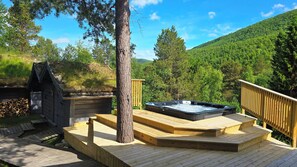 Un jacuzzi en una terraza de madera con vistas a una ladera boscosa.