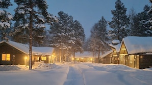 A snow-covered pathway leading to a row of log cabins with warm lights, surrounded by snow-laden trees. - ONGA Boutique Lodge (Alta)