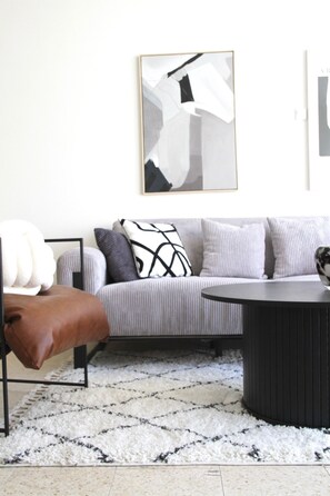 A modern living room with a grey sofa, a brown leather armchair, a black coffee table, and a patterned rug. - Charming Old North near Park by FeelHome (Tel Aviv)