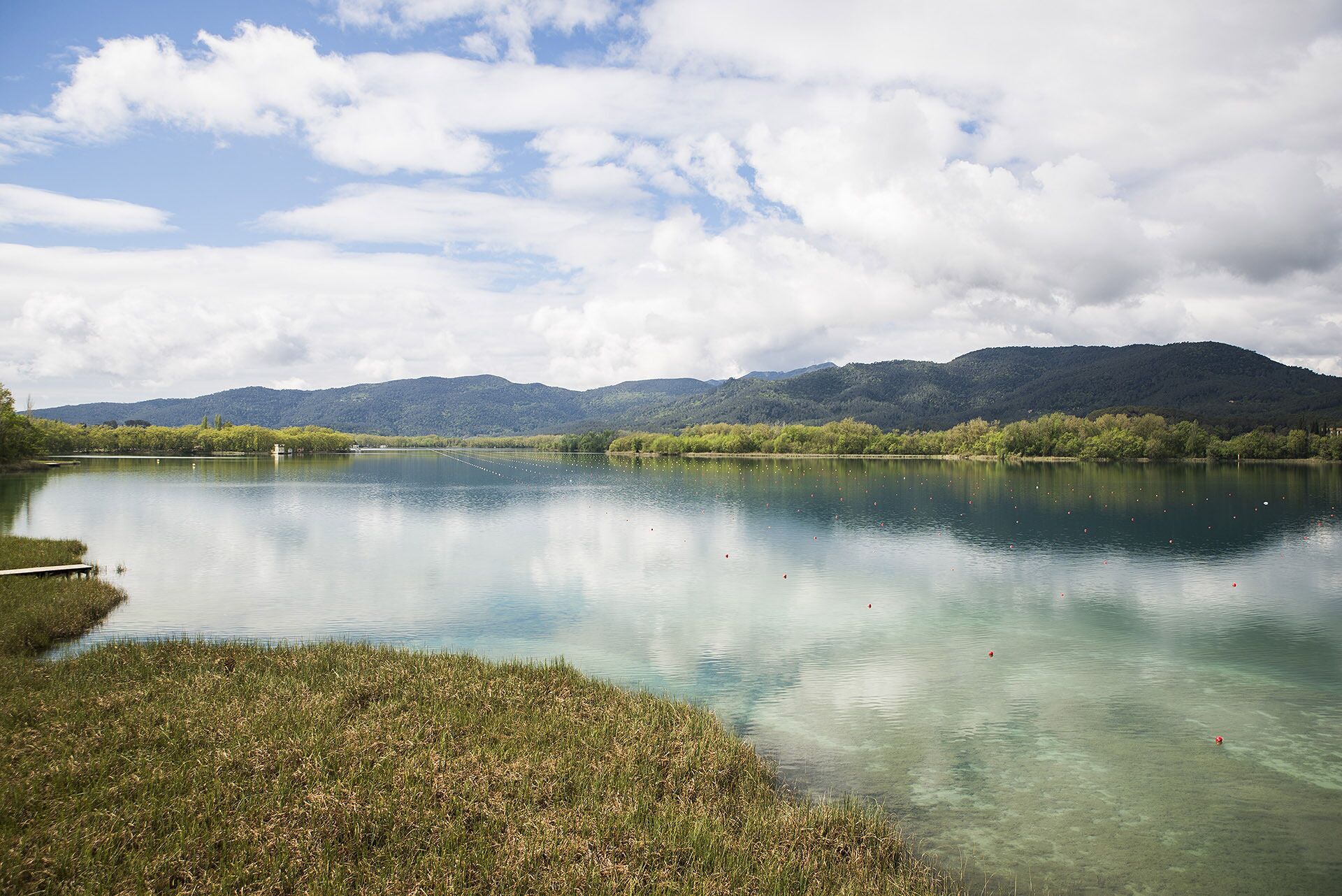 Un lago tranquilo con aguas cristalinas, rodeado de abundante vegetación y montañas a la distancia.