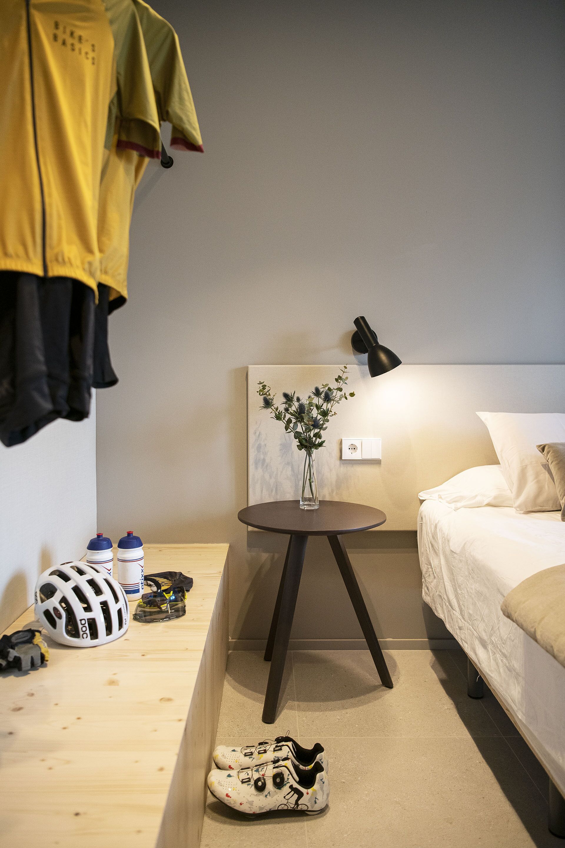 Una habitación de hotel con cama, mesita de noche y lámpara de pared.