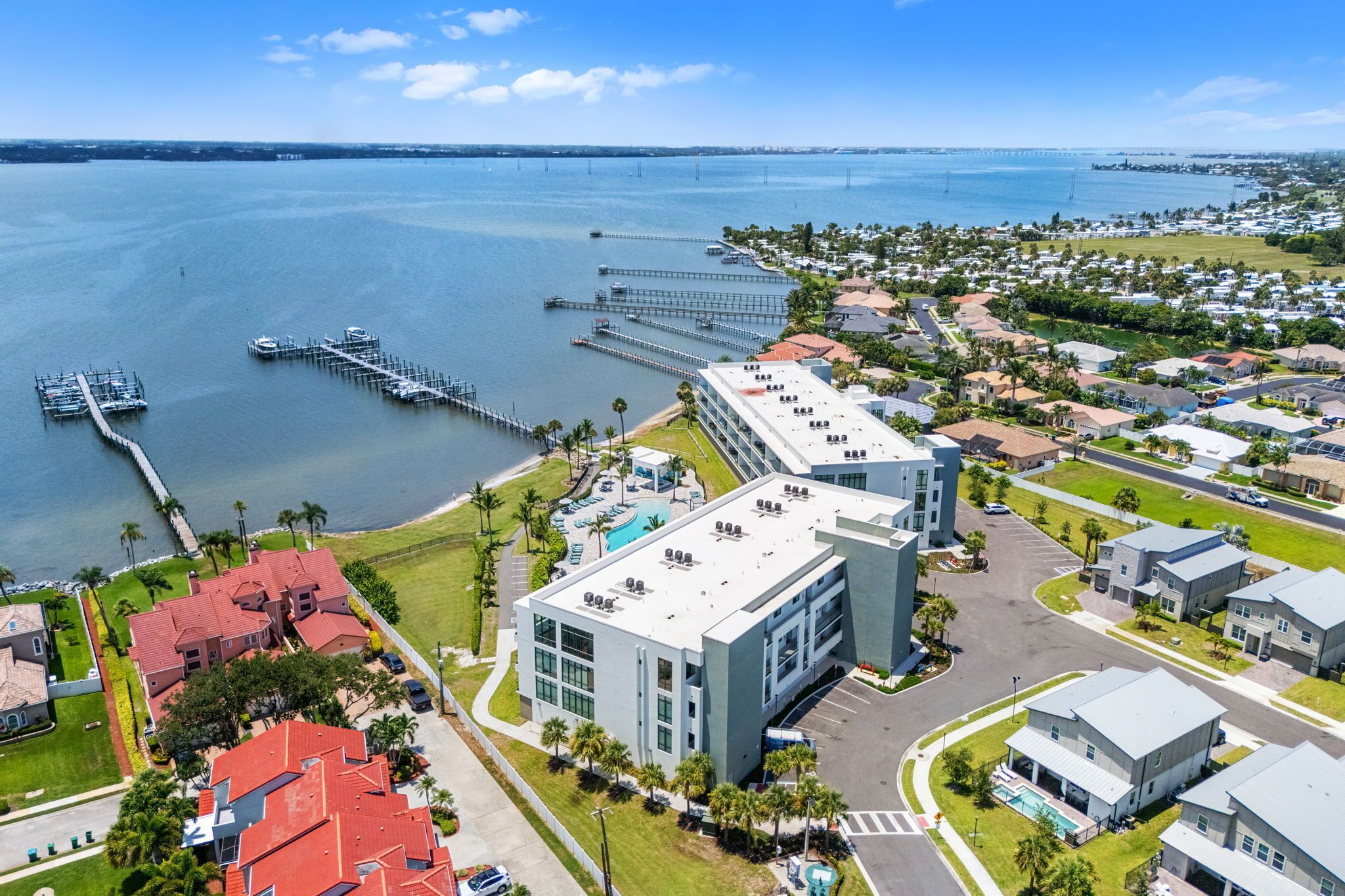 An aerial view of a coastal residential area with a marina, modern buildings, and a large body of water.