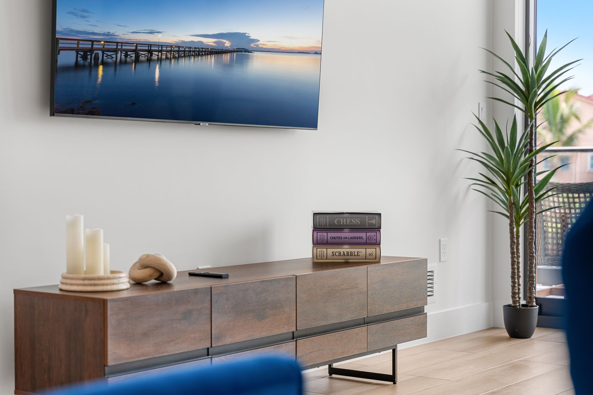 Un salon moderne avec un téléviseur à écran plat fixé au mur, une console en bois agrémentée d’objets décoratifs et une plante en pot.