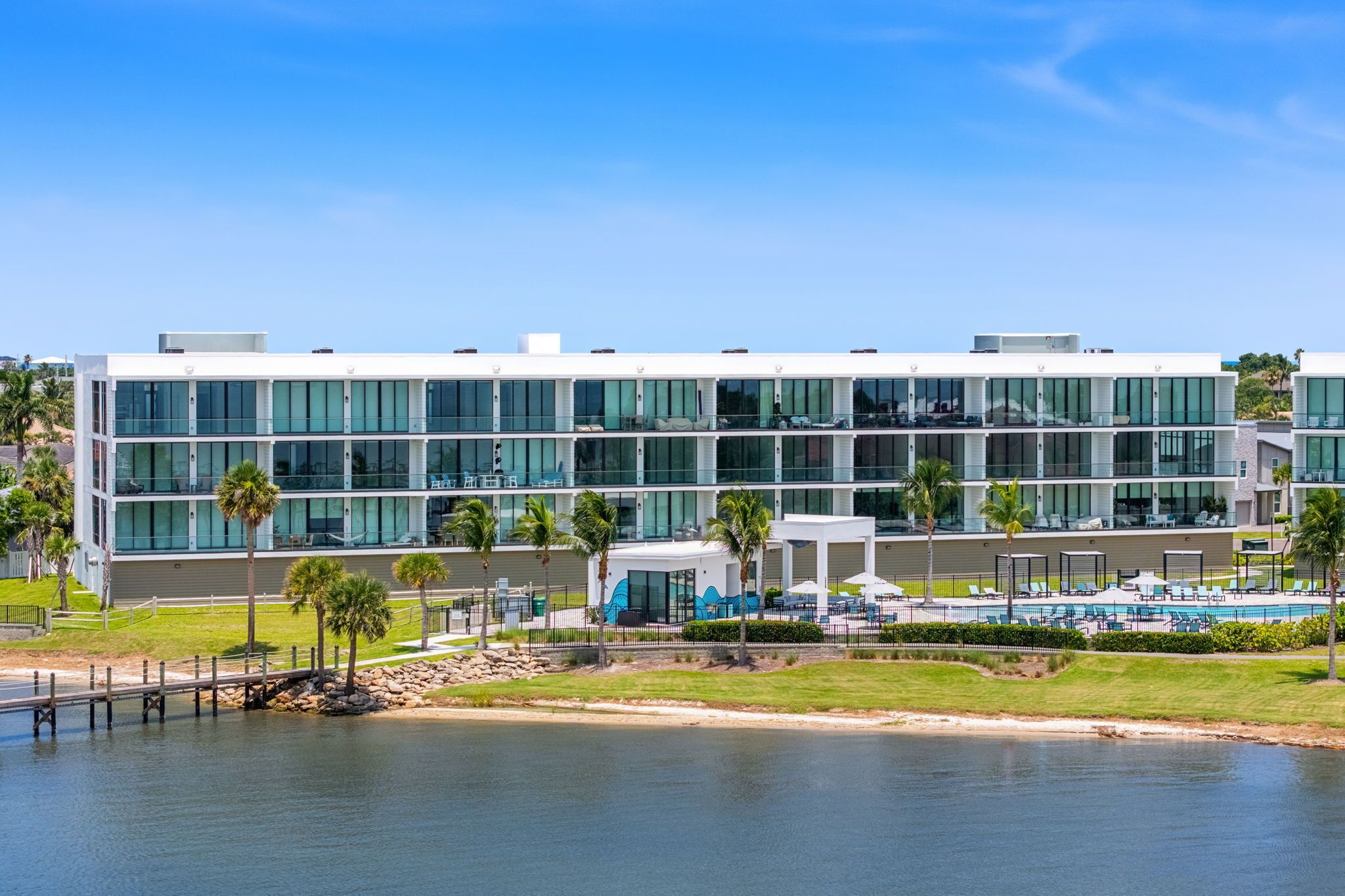 A modern hotel with a glass facade, a pool area, and a view of the water.