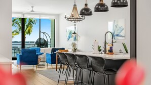 Ett modernt kök med en central köksö, barstolar, hängande lampor och utsikt över havet.