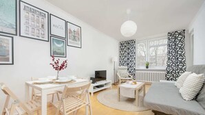 A modern living room with a dining area, white walls, and a grey sofa. - Comfortable Apartment | Balcony | Close to the Center (Warszawa)