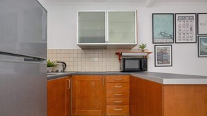A kitchen with wooden cabinets, a stainless steel refrigerator, a microwave, and a tiled backsplash. - Comfortable Apartment | Balcony | Close to the Center (Warszawa)