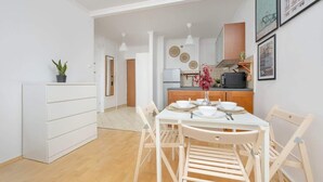 A compact kitchen with white cabinets, a dining table with chairs, and a small potted plant. - Comfortable Apartment | Balcony | Close to the Center (Warszawa)