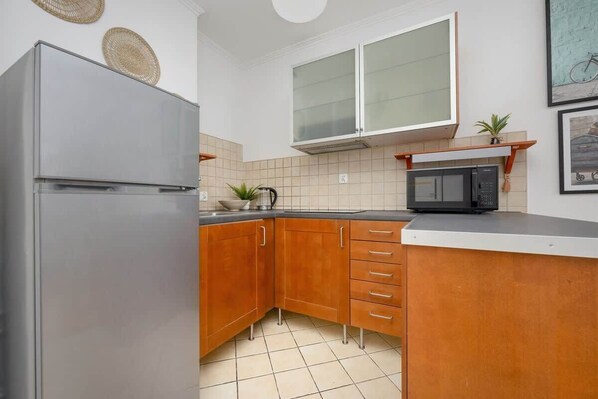 A kitchen with wooden cabinets, a stainless steel refrigerator, a microwave, and a tiled backsplash.