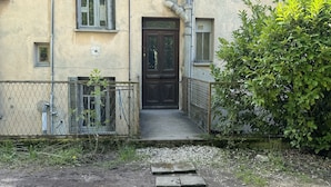 Rakennuksessa on tumma puinen ovi, pieni kuisti ja metallinen ketjulanka-aita.