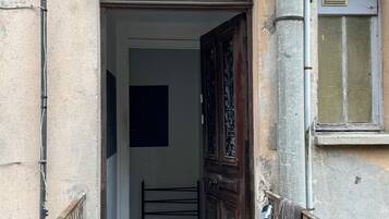 Un ingresso stretto con un cancello in metallo, una porta in legno finemente intagliata e un piccolo contenitore metallico a terra.