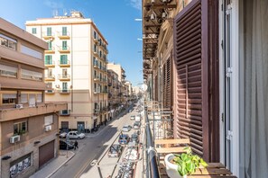 A narrow street with buildings on either side, a balcony with a plant, and parked cars. - Mika Apartment Alla Stazione (Palermo)