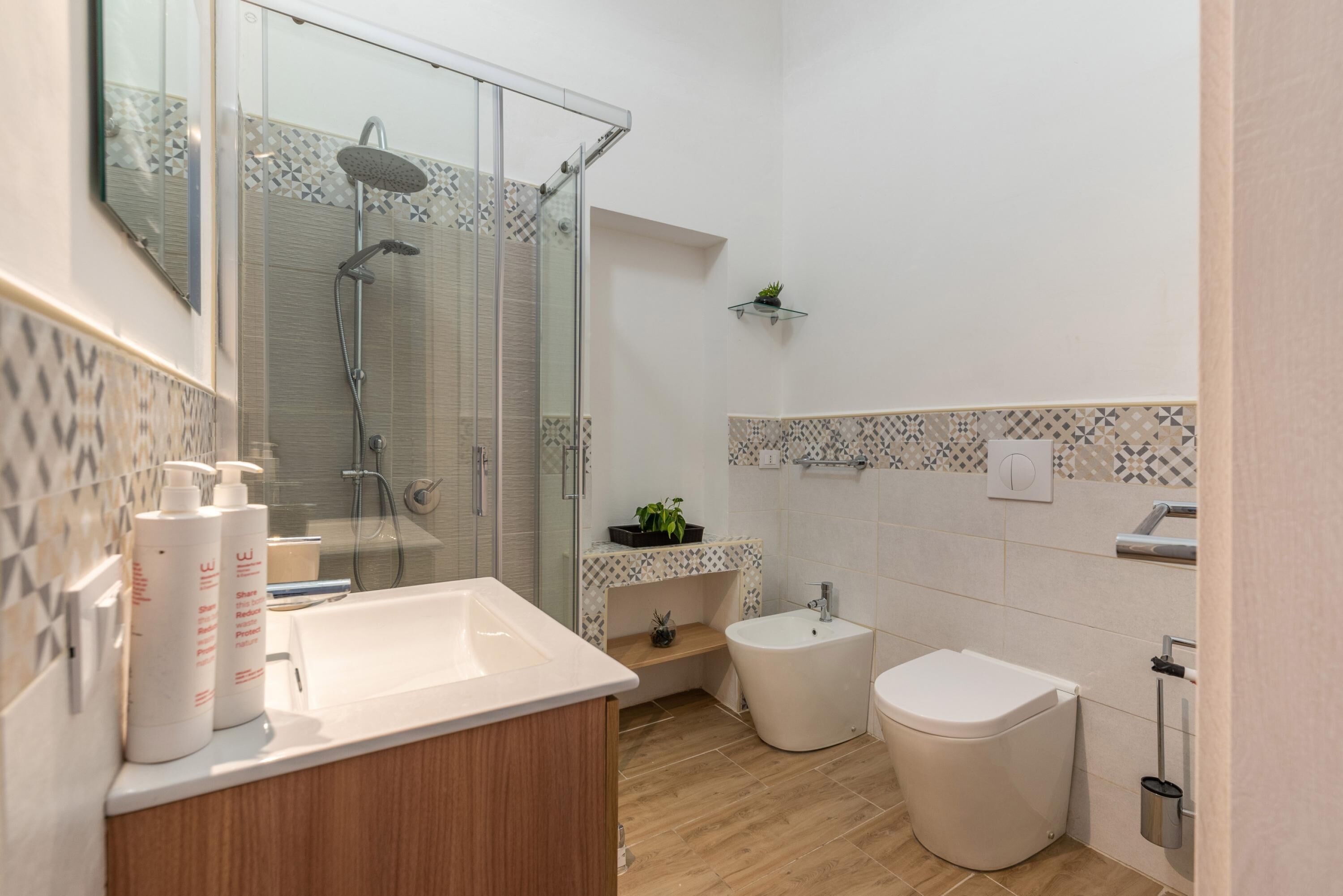 Et moderne badeværelse med glasbrusekabine, vask med toiletartikler, en bidet og et toilet.