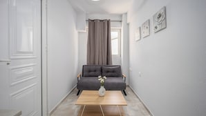 A hallway with a grey sofa, a white vase with flowers, and a wooden coffee table. - Sun City Apartments by Estia (Agios Nikolaos)