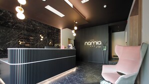 Ein moderner Hotel-Empfangsbereich mit einem Marmor-Empfangstresen, einem pinken Lounge-Sessel und einem an der Wand befestigten Schild mit der Aufschrift 'HOTEL namia'.