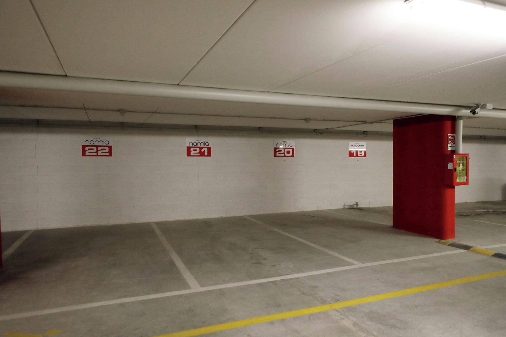 Un parcheggio sotterraneo con posti auto numerati, un pilastro rosso e un estintore.