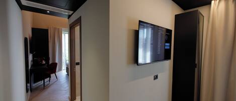 Una habitación de hotel moderna con un televisor de pantalla plana montado en la pared, piso de madera y una puerta con cortinas.