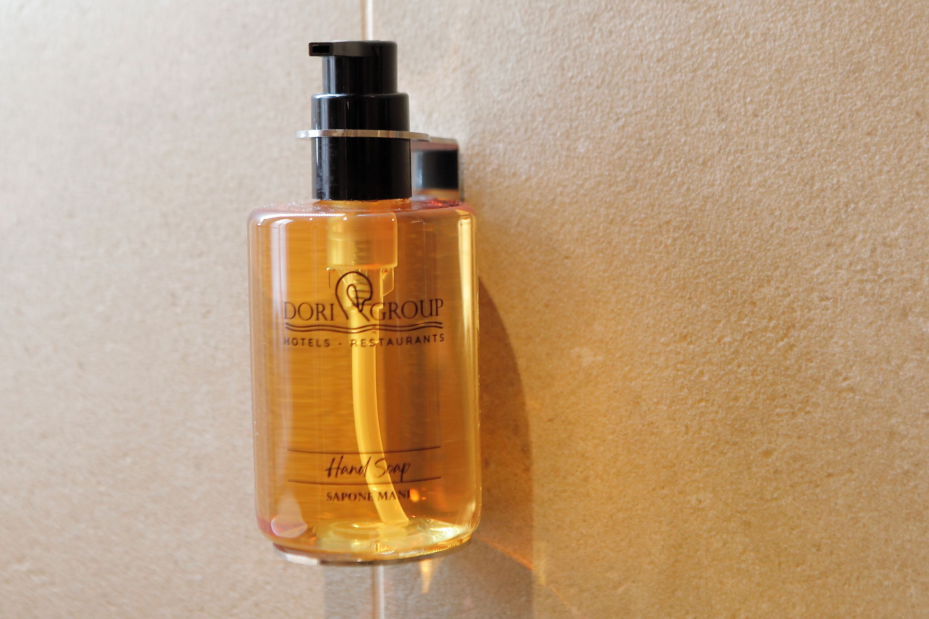 A bottle of hand soap labeled "DORIGROUP Hotels - Restaurants" against a textured wall.