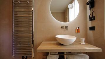 A modern bathroom with a large oval mirror, a round sink, a towel rack, and a hairdryer mounted on the wall.